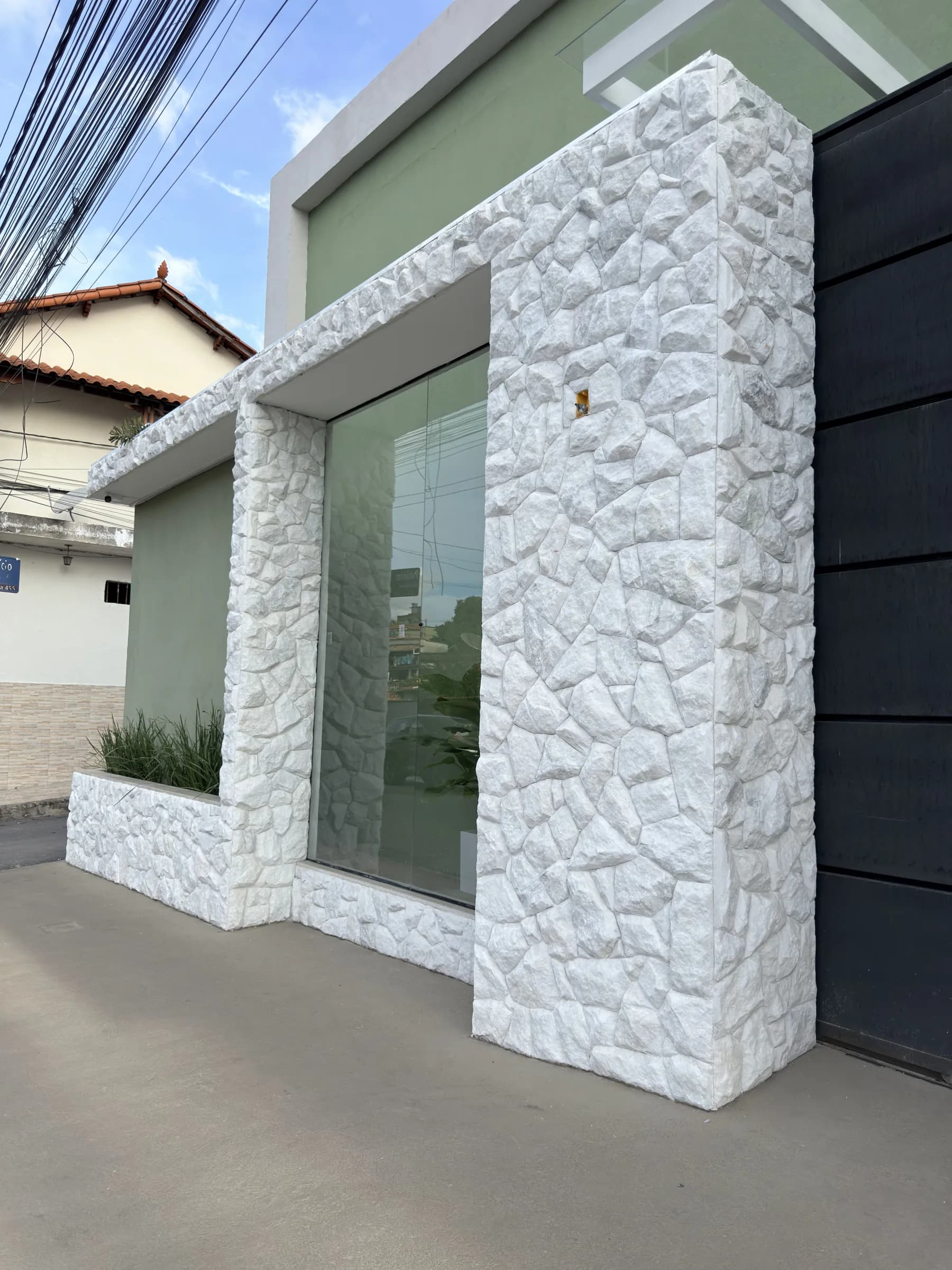 Fachada da Dondoka Recepções durante o dia, com revestimento em pedra branca e portão escuro